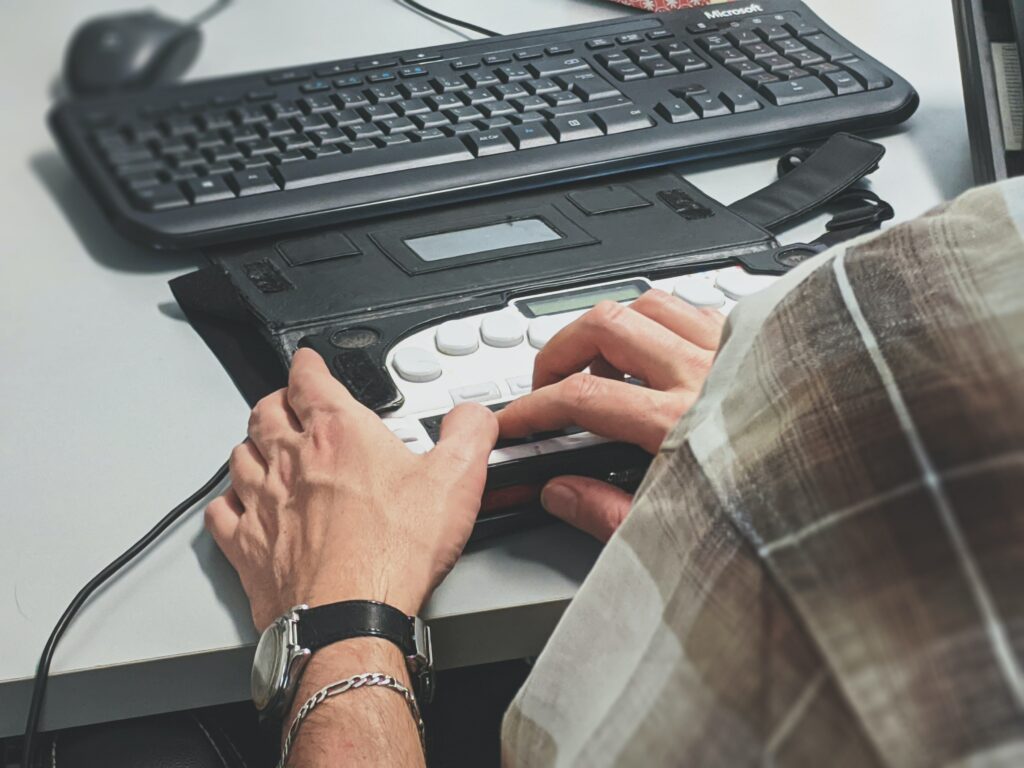 Henkilön kädet ja tietokoneen näppäimistö, mukana myös  tietokoneapuväline. 