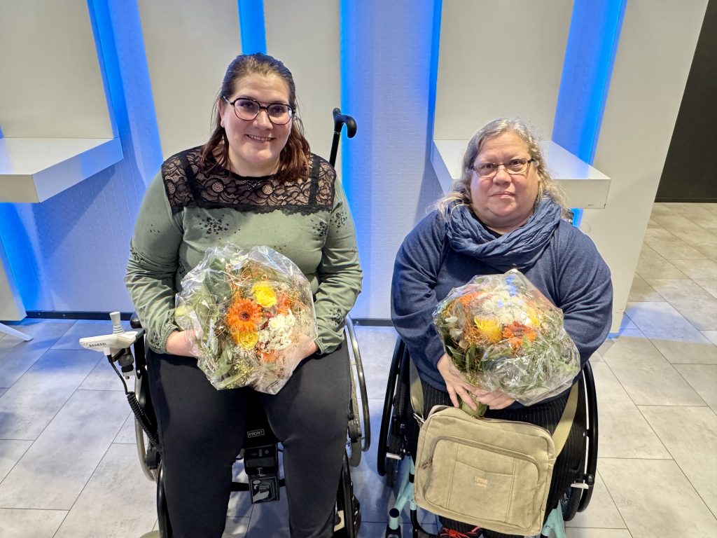 Elina ja Satu-Maria kukkakimput sylissään. Molemmat istuvat pyörätuolissa.