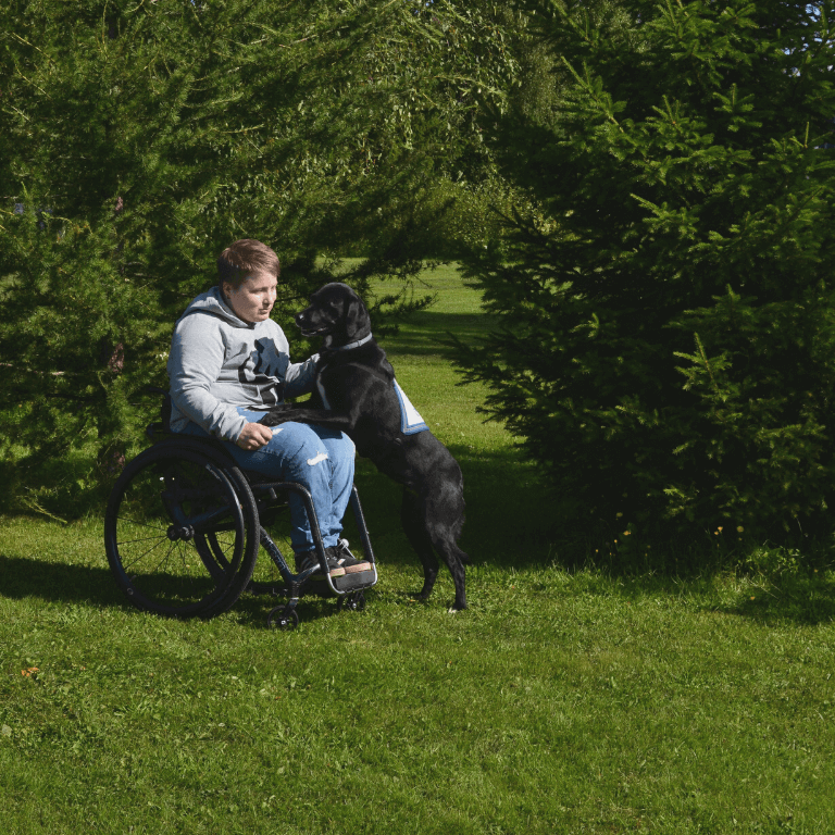 Marja Hukkanen istuu pyörätuolissa, vieressä avustajakoira.