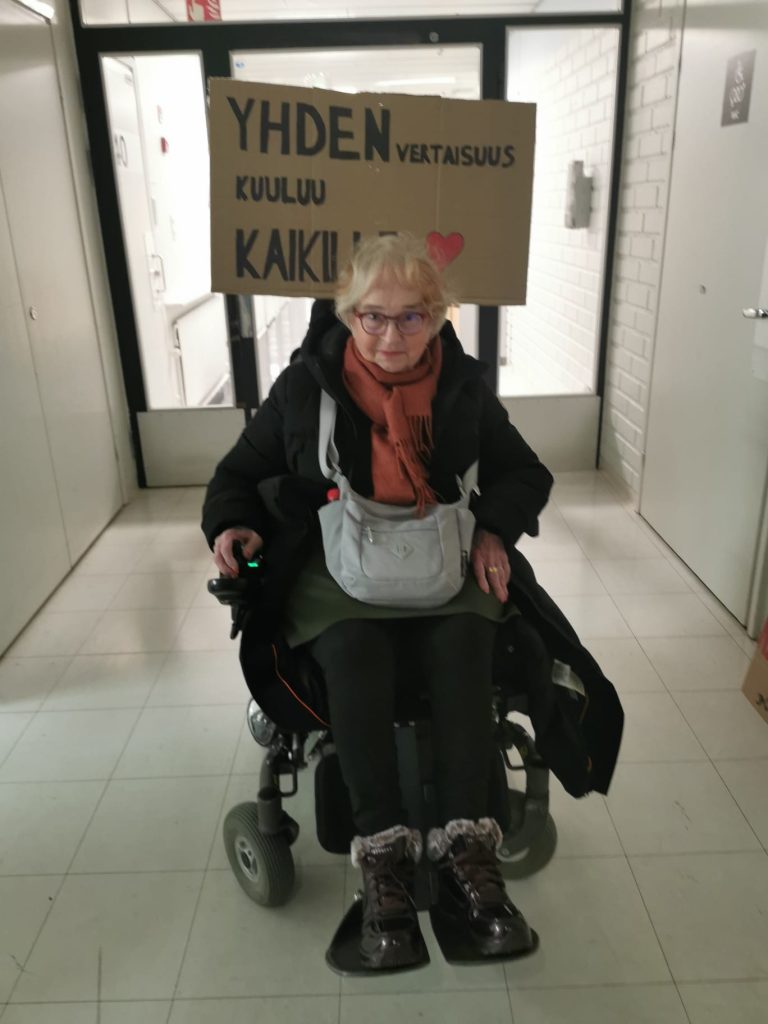 Nainen pyöräyuolissa. Takana mielenosoituskyltti: Yhdenvertaisuus kuuluu kaikille.