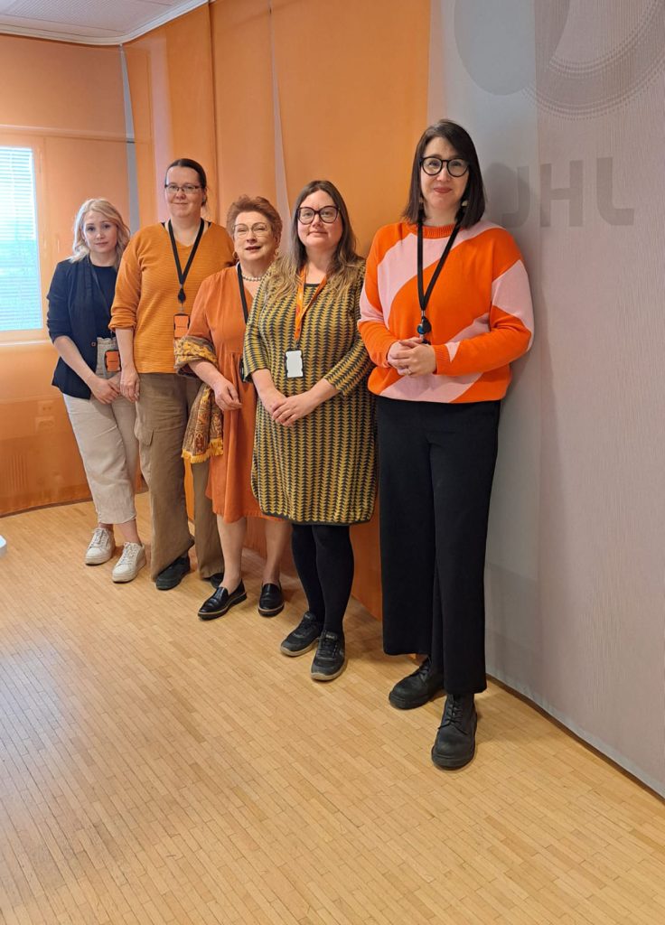 Viisi TES-neuvottelijaa seisoo seinän edessä.