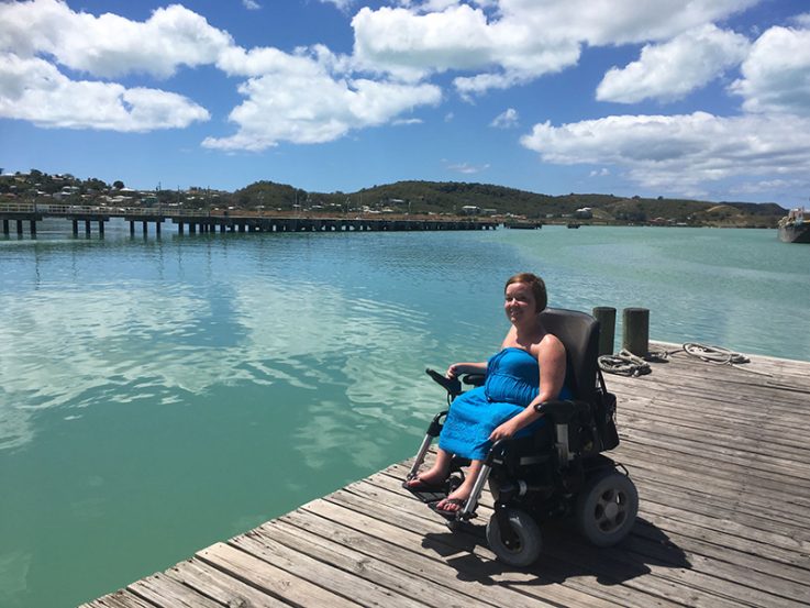 Palmuasema-blogin kirjoittaja Sanna Kalmari istuu sähköpyörätuolissa laiturilla turkoosin meren äärellä.