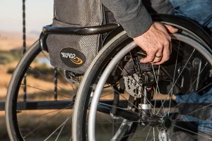 Kuvassa on lähikuvassa pyörätuolissa oleva mieshenkilö. Kuvassa näkyy vain pyörätuolin takaosa, rengas ja rengaasta kiinnipitävä käsi.